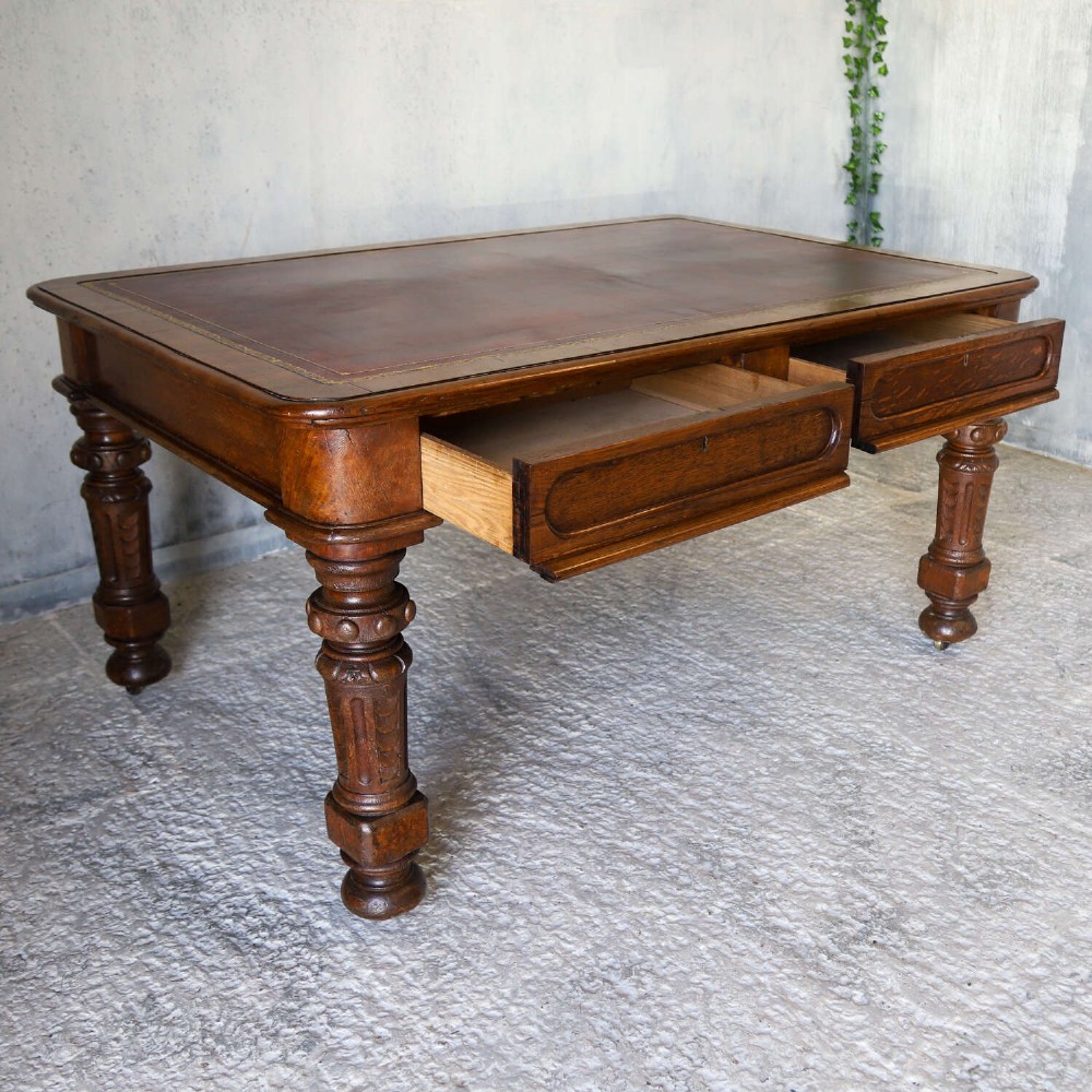 A 19th-century English oak Gothic Revival library table featuring an inset leather top and carved turned legs on brass castors. View VI