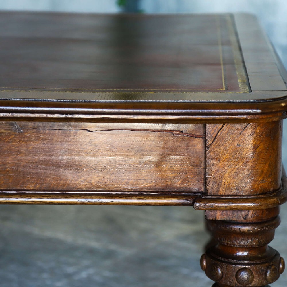 A 19th-century English oak Gothic Revival library table featuring an inset leather top and carved turned legs on brass castors. View VIII