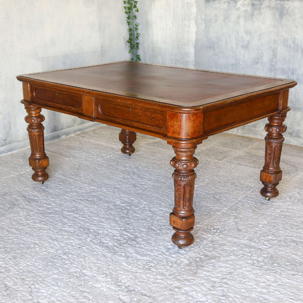 A 19th-century English oak Gothic Revival library table featuring an inset leather top and carved turned legs on brass castors. View XI