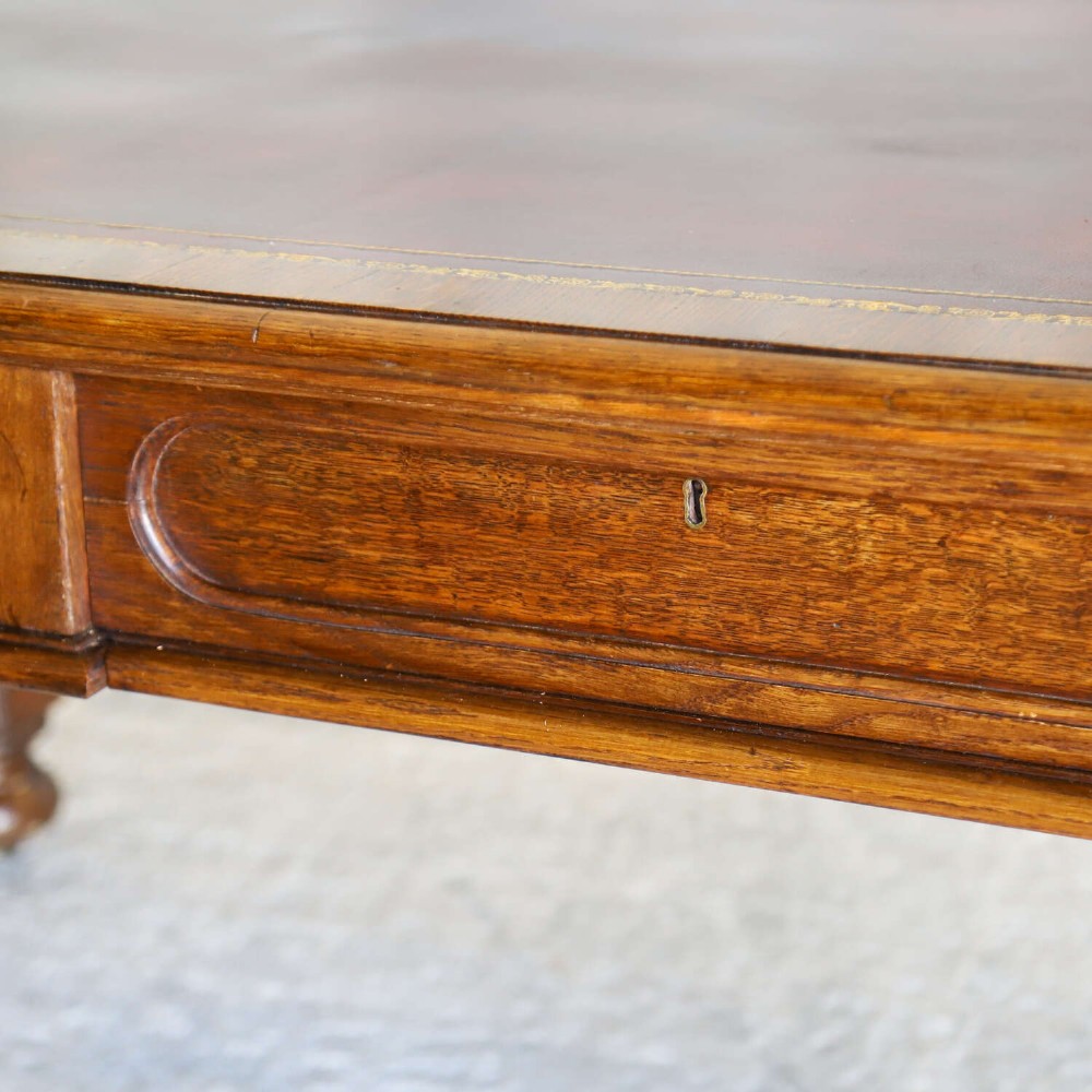 A 19th-century English oak Gothic Revival library table featuring an inset leather top and carved turned legs on brass castors. View XII