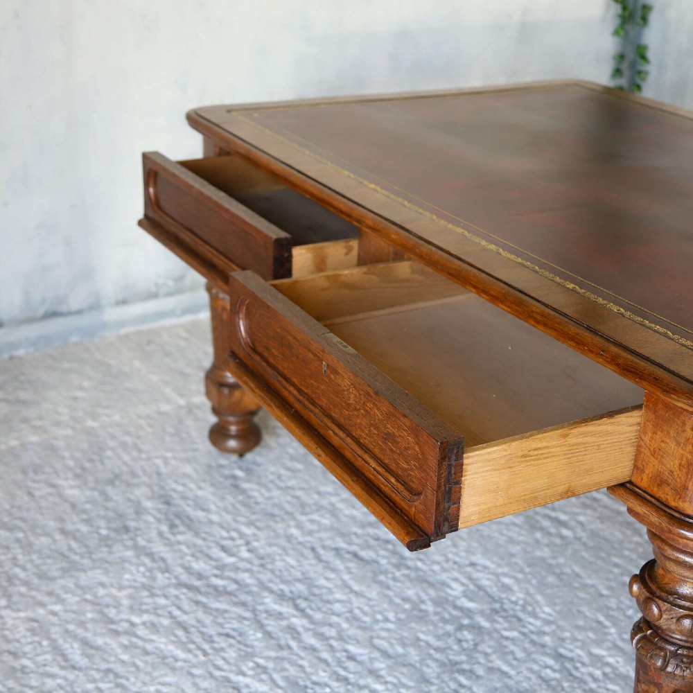 A 19th-century English oak Gothic Revival library table featuring an inset leather top and carved turned legs on brass castors. View XIII