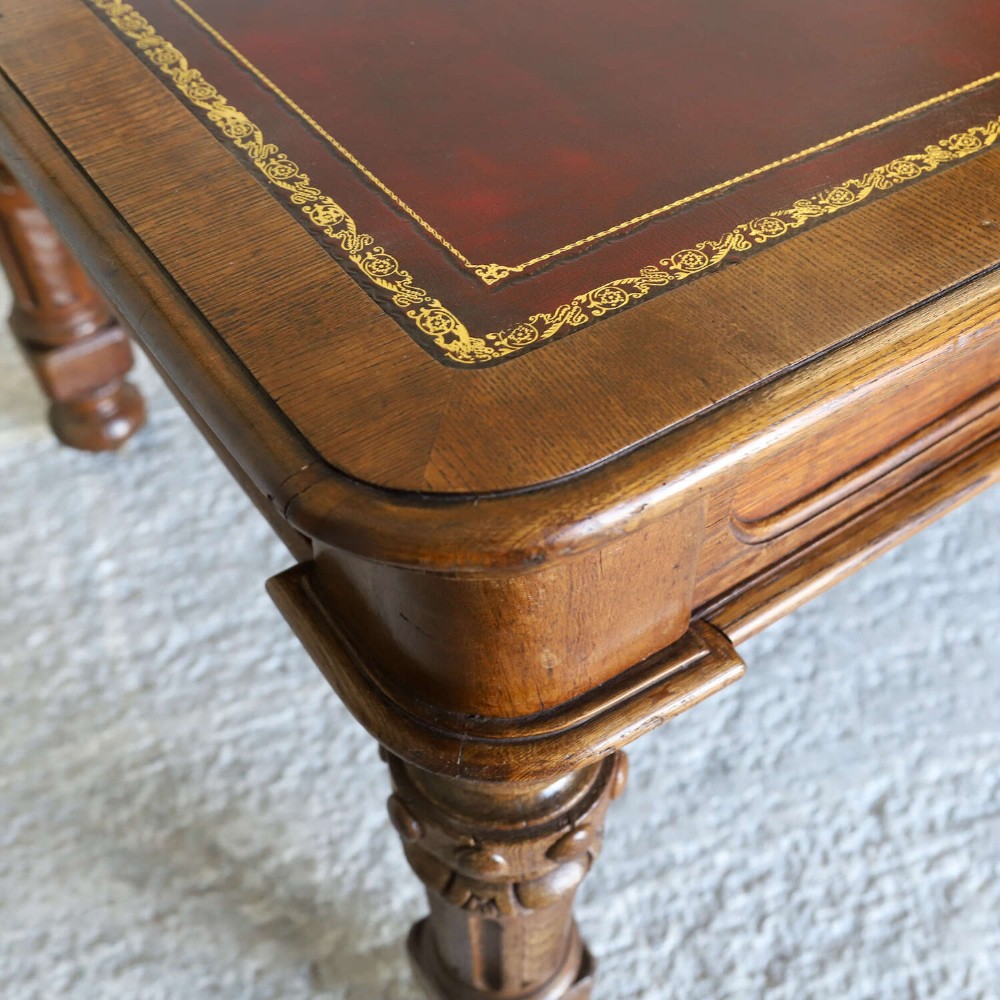 A 19th-century English oak Gothic Revival library table featuring an inset leather top and carved turned legs on brass castors. View XV