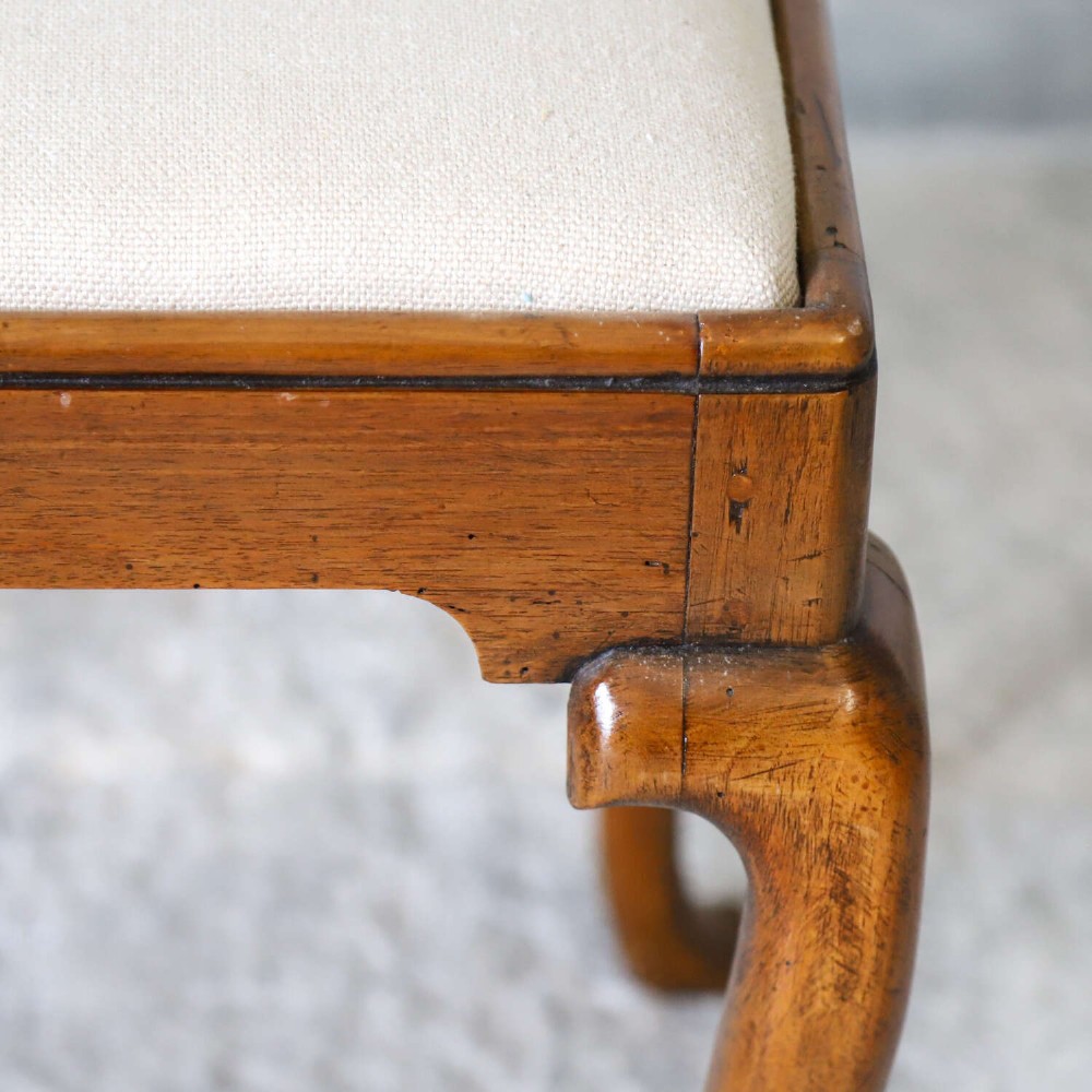 An early eighteenth-century George I walnut stool featuring four shaped cabriole legs and a cream upholstered drop-in seat. View VI