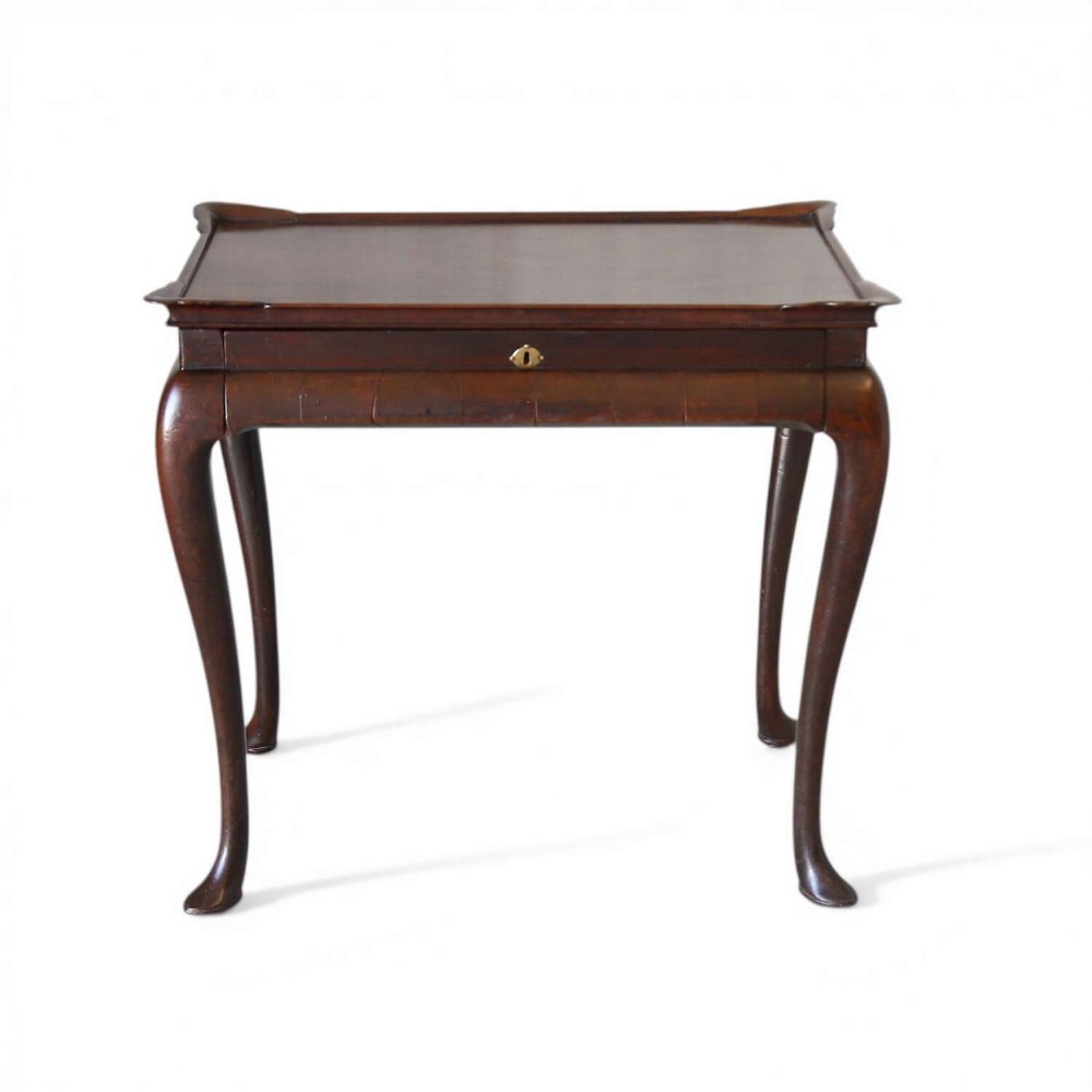 An early Georgian dark Cuban mahogany silver table featuring a raised tray top rim, single drawer with brass escutcheon, and slender cabriole legs terminating in pad feet.