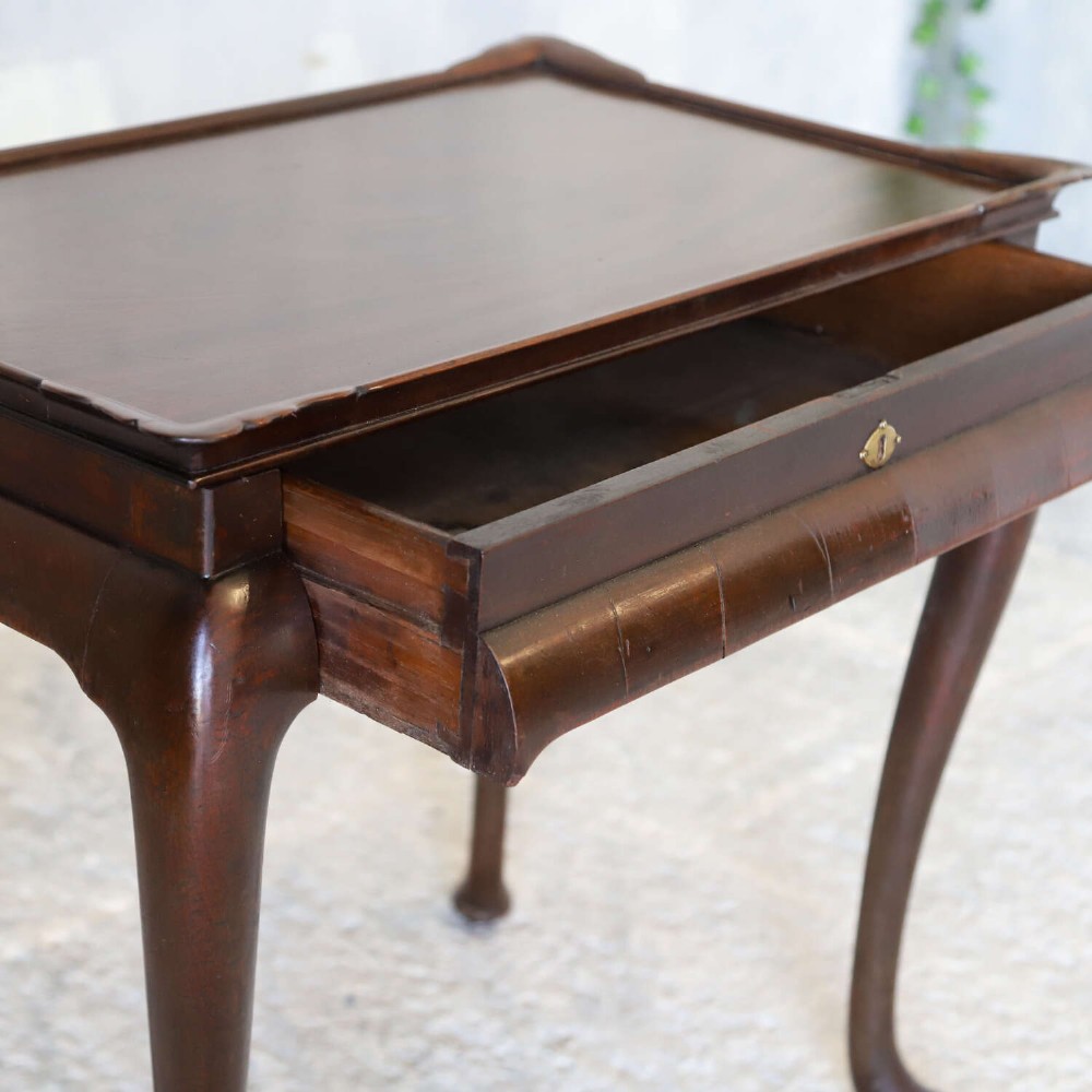 An early Georgian dark Cuban mahogany silver table featuring a raised tray top rim, single drawer with brass escutcheon, and slender cabriole legs terminating in pad feet. View II