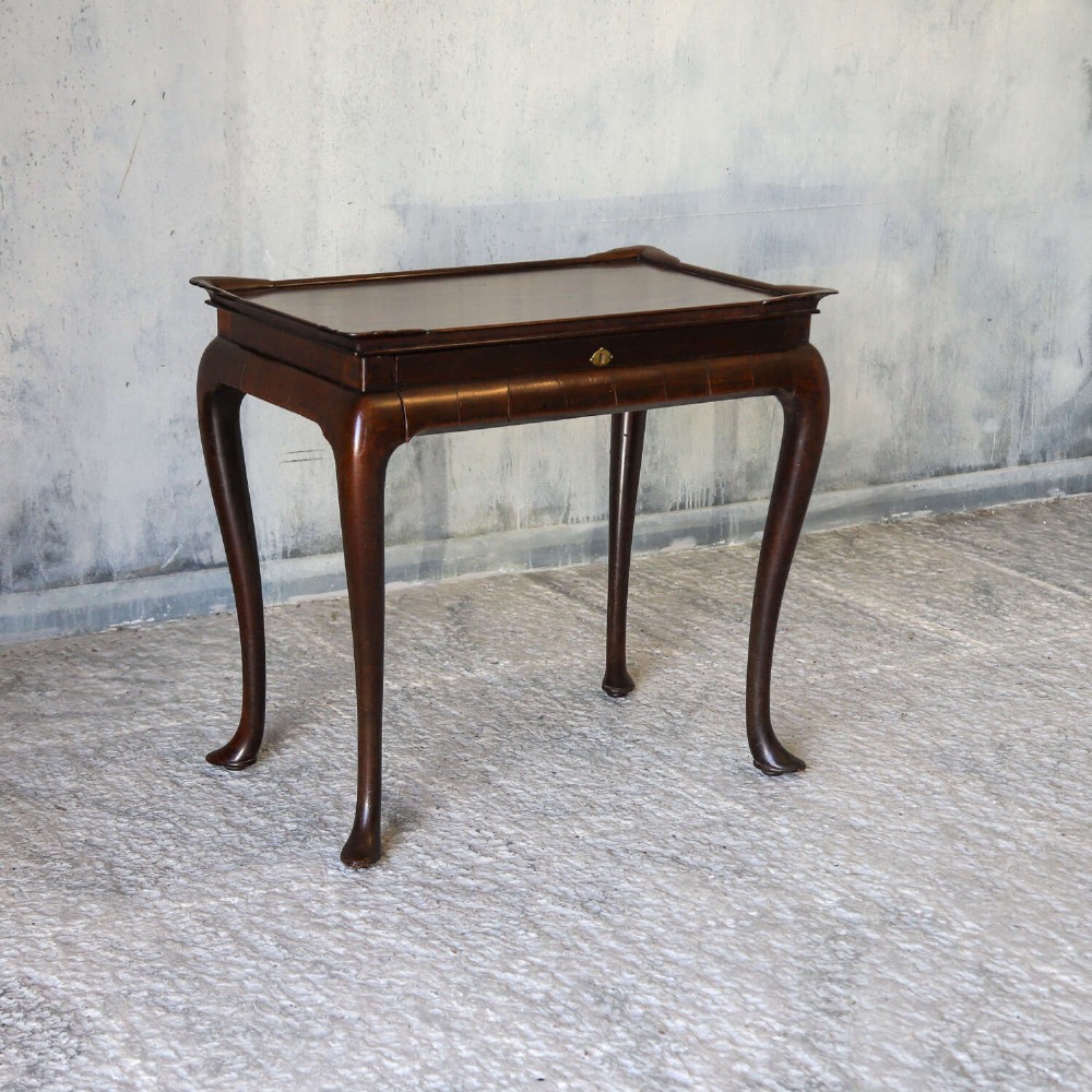 An early Georgian dark Cuban mahogany silver table featuring a raised tray top rim, single drawer with brass escutcheon, and slender cabriole legs terminating in pad feet. View IV