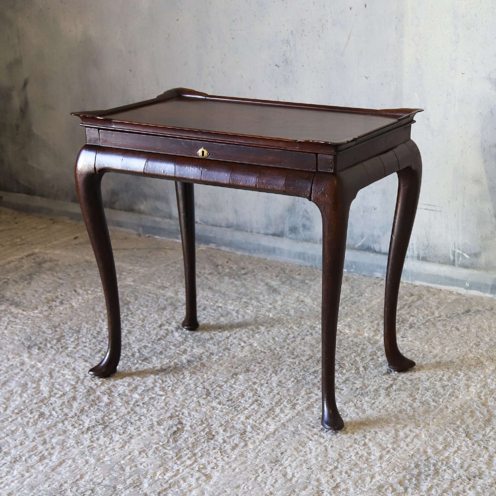 An early Georgian dark Cuban mahogany silver table featuring a raised tray top rim, single drawer with brass escutcheon, and slender cabriole legs terminating in pad feet. View V