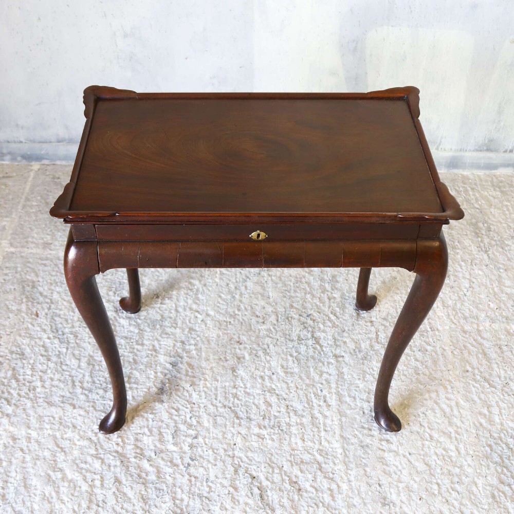 An early Georgian dark Cuban mahogany silver table featuring a raised tray top rim, single drawer with brass escutcheon, and slender cabriole legs terminating in pad feet. View VI