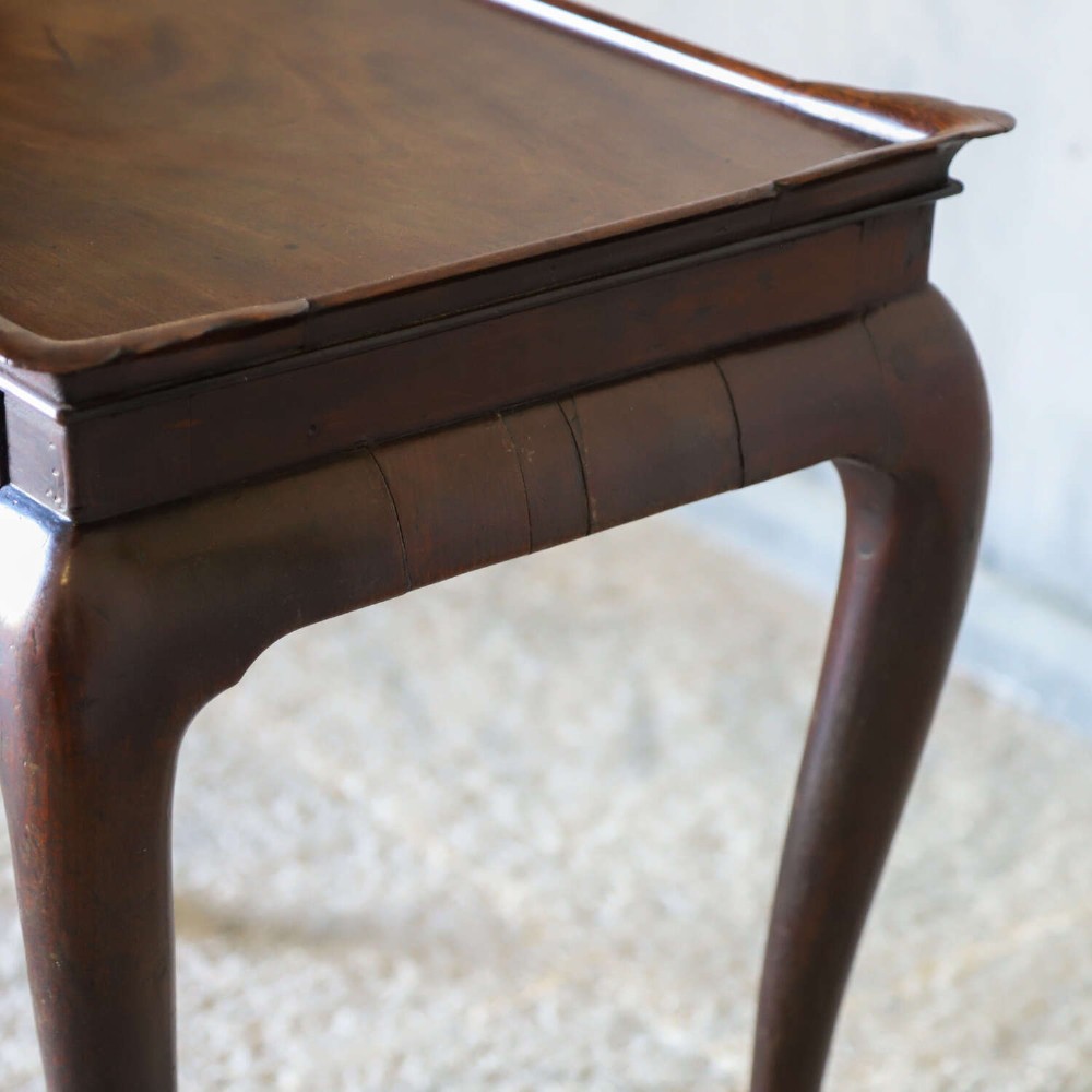 An early Georgian dark Cuban mahogany silver table featuring a raised tray top rim, single drawer with brass escutcheon, and slender cabriole legs terminating in pad feet. View XI