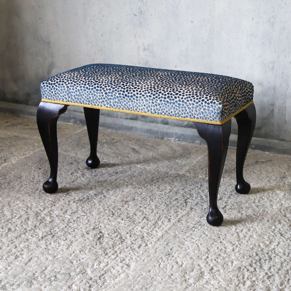 An Edwardian style ebonised wooden stool with curved cabriole legs, pad feet, gold trim braid, and a patterned blue upholstered top. View III