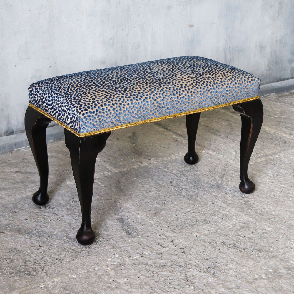An Edwardian style ebonised wooden stool with curved cabriole legs, pad feet, gold trim braid, and a patterned blue upholstered top. View IV