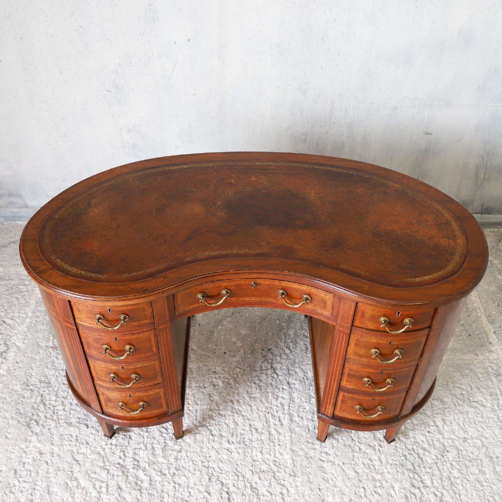 A late eighteenth-century Sheraton Revival mahogany kidney-shaped writing desk featuring a gilt-tooled leather top, nine drawers with brass handles, and line inlay. View V