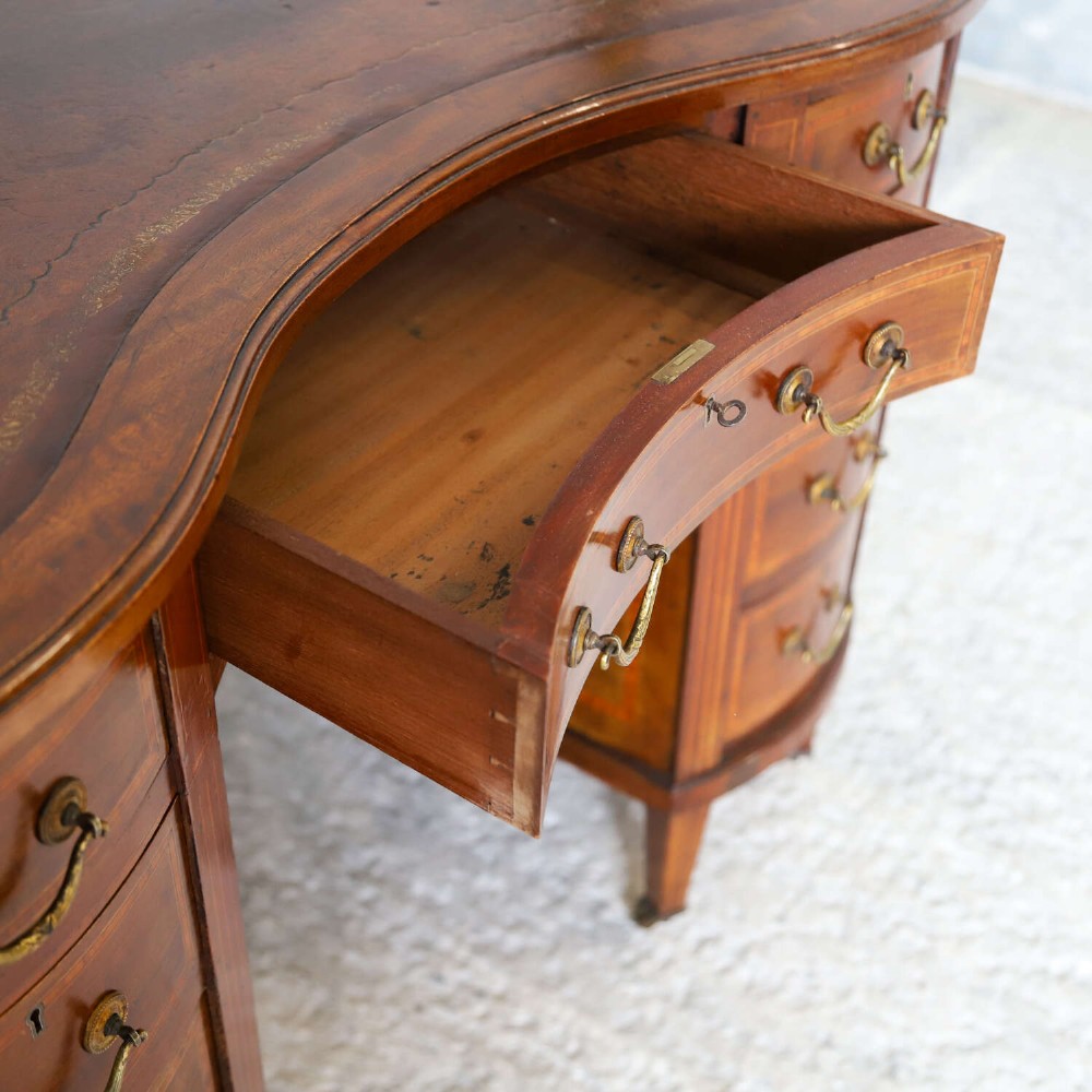 A late eighteenth-century Sheraton Revival mahogany kidney-shaped writing desk featuring a gilt-tooled leather top, nine drawers with brass handles, and line inlay. View X