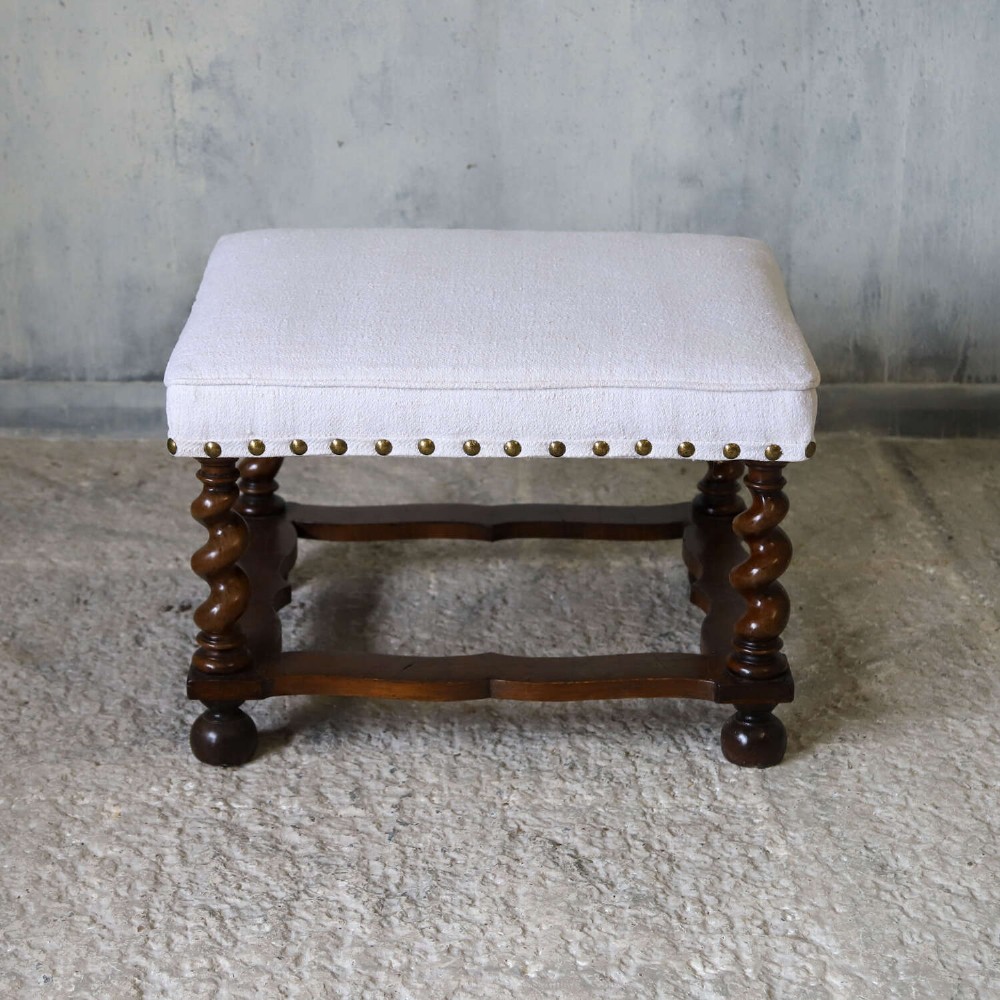 A square upholstered stool with neutral fabric and brass nailhead trim, supported by dark turned barley-twist legs and a serpentine stretcher on ball feet. View II