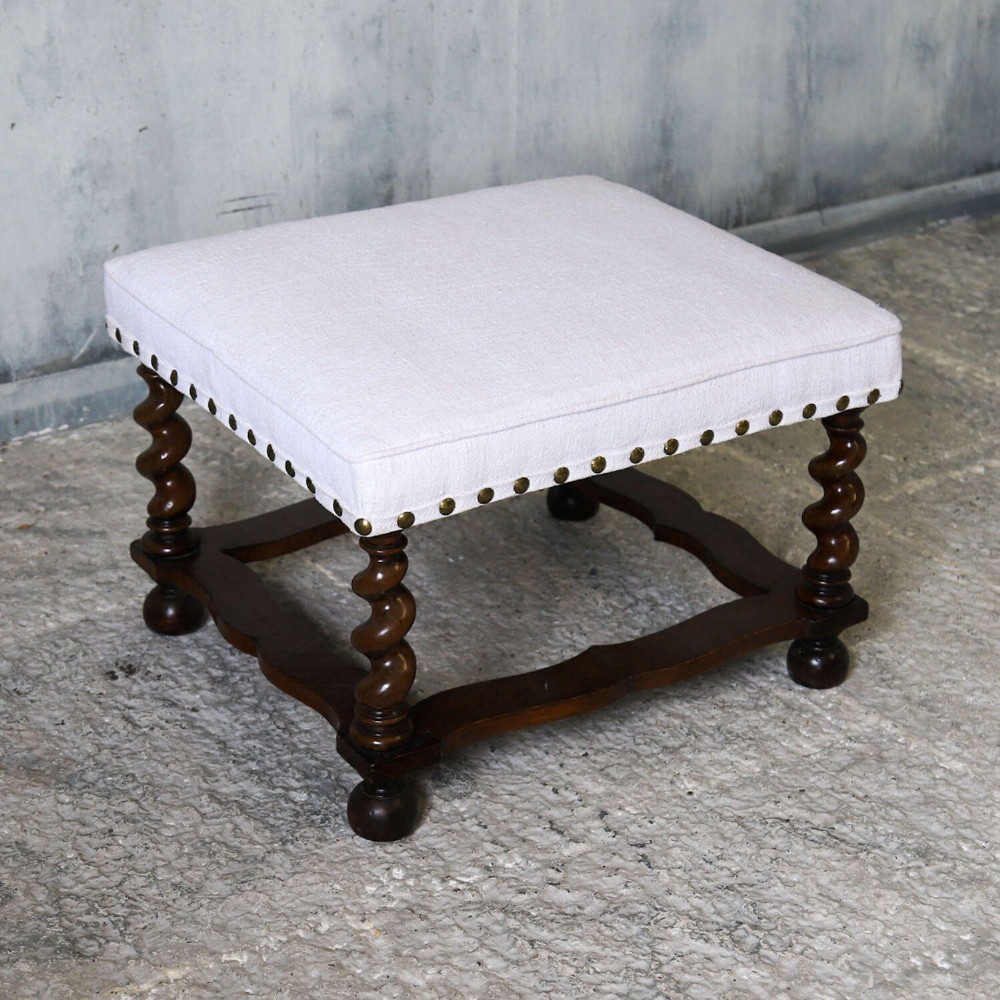 A square upholstered stool with neutral fabric and brass nailhead trim, supported by dark turned barley-twist legs and a serpentine stretcher on ball feet. View IV