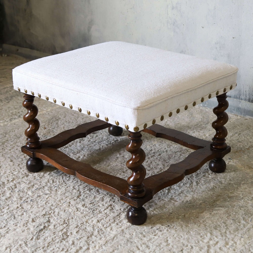 A square upholstered stool with neutral fabric and brass nailhead trim, supported by dark turned barley-twist legs and a serpentine stretcher on ball feet. View VIII