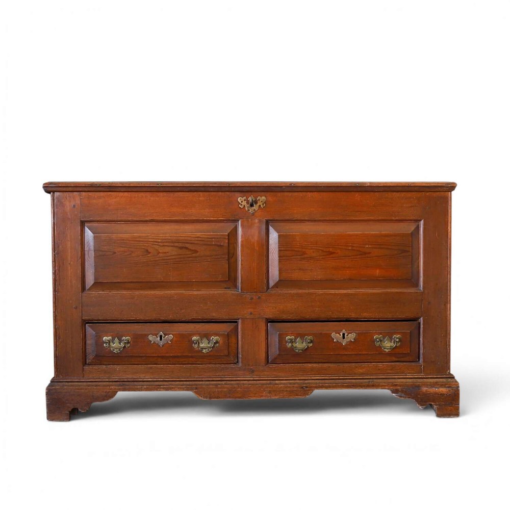 An 18th-century pine mule chest with two raised front panels, two lower drawers, and original brass hardware on a bracket base.