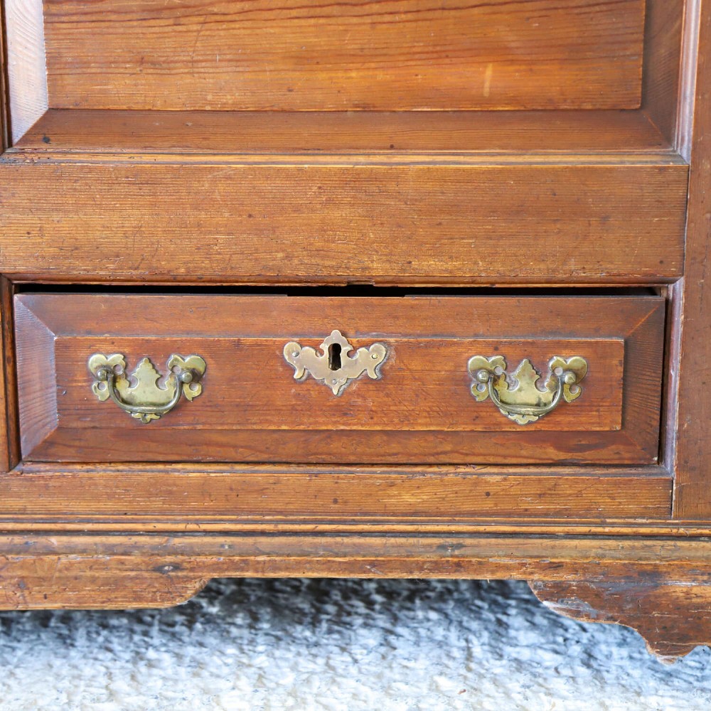 An 18th-century pine mule chest with two raised front panels, two lower drawers, and original brass hardware on a bracket base. View VI