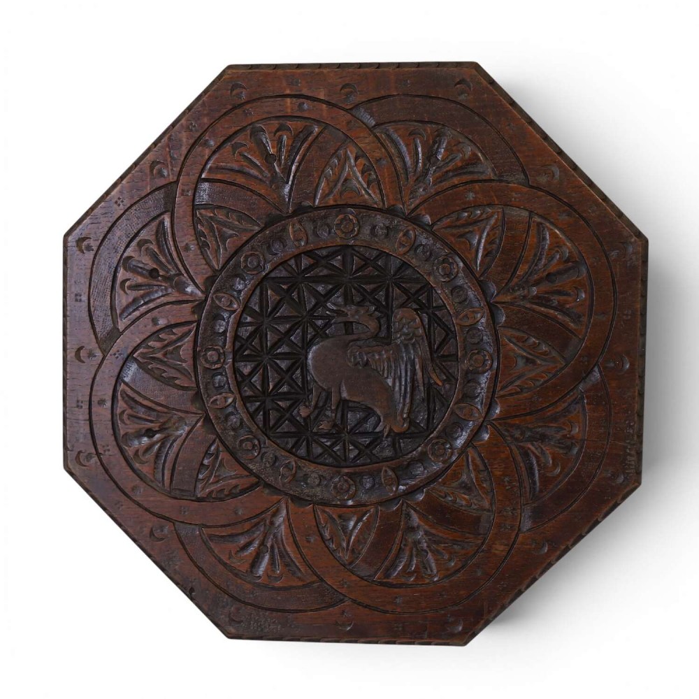 An octagonal dark carved oak panel featuring a central winged mythical creature within geometric latticework and leaf motifs.