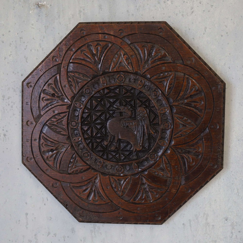 An octagonal dark carved oak panel featuring a central winged mythical creature within geometric latticework and leaf motifs. View II