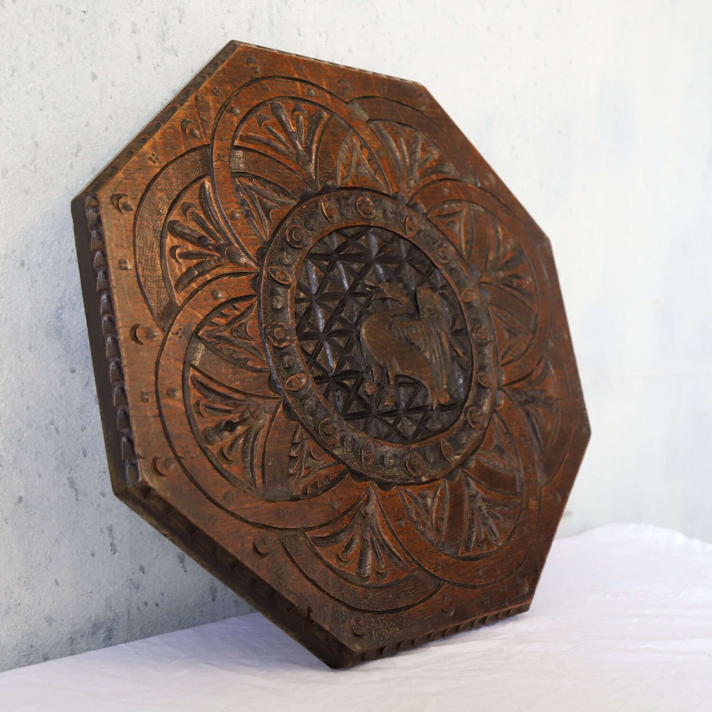 An octagonal dark carved oak panel featuring a central winged mythical creature within geometric latticework and leaf motifs. View IV