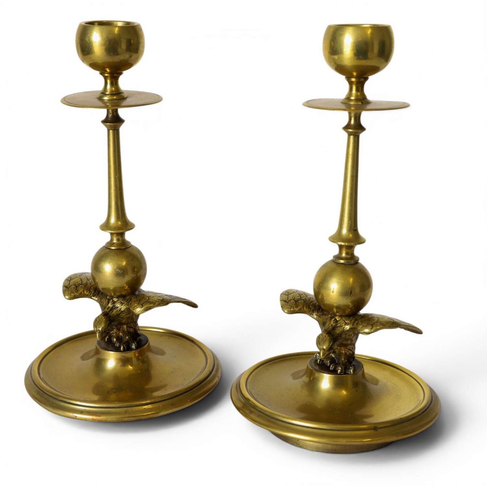 A pair of Georgian brass candlesticks featuring spread-winged eagle motifs supporting tapering stems above circular dished bases.