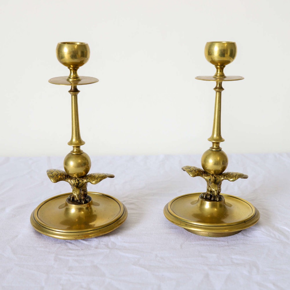 A pair of Georgian brass candlesticks featuring spread-winged eagle motifs supporting tapering stems above circular dished bases. View II