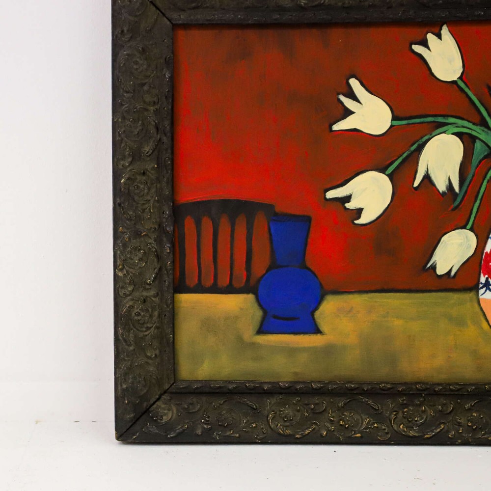 A 1930s Swedish still life oil painting depicting white tulips in a patterned ceramic vase next to a blue jug on a red background, set inside a carved dark wooden frame. View III