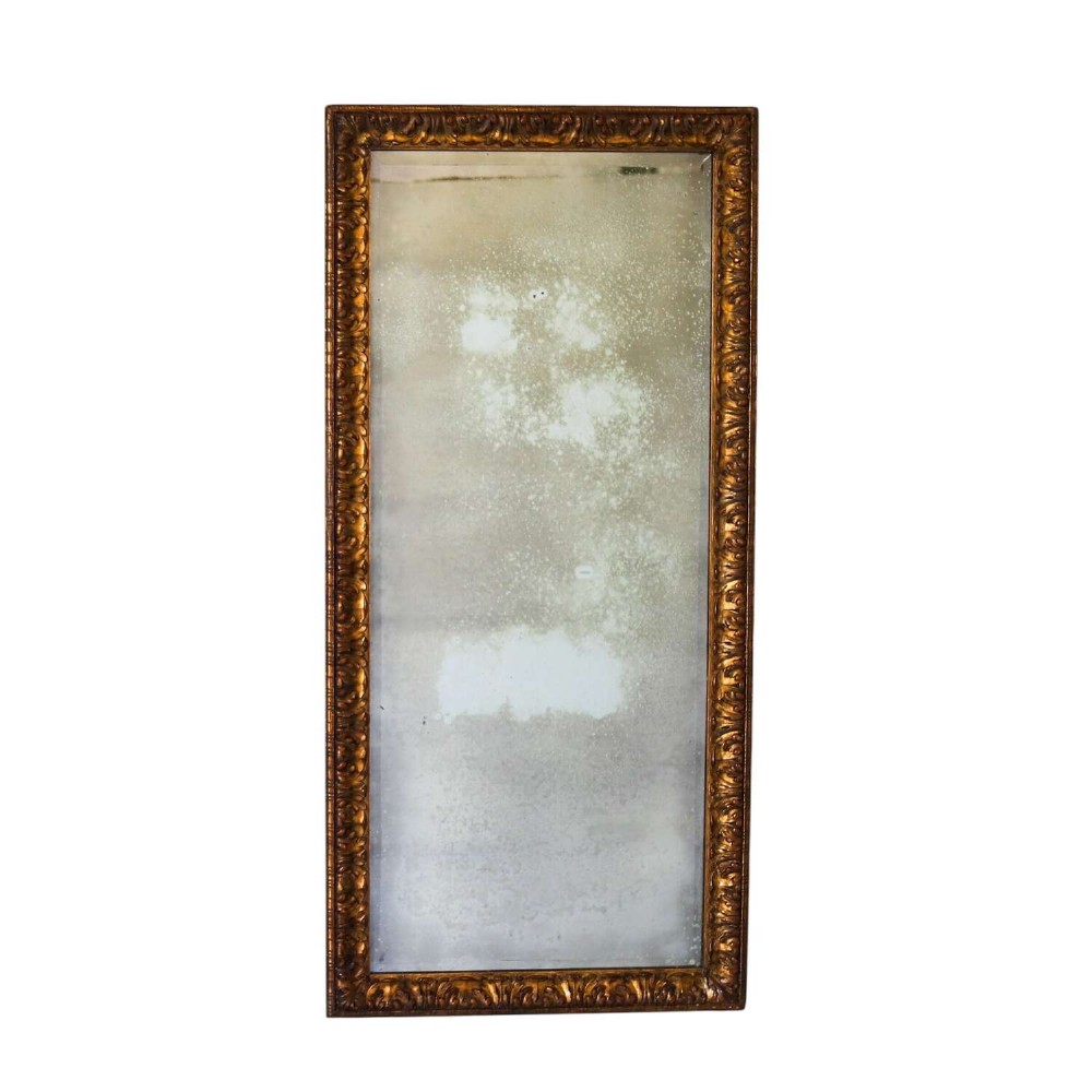 A tall rectangular nineteenth-century French mirror featuring a gilded wood frame with relief pattern molding and heavily foxed mirrored glass.