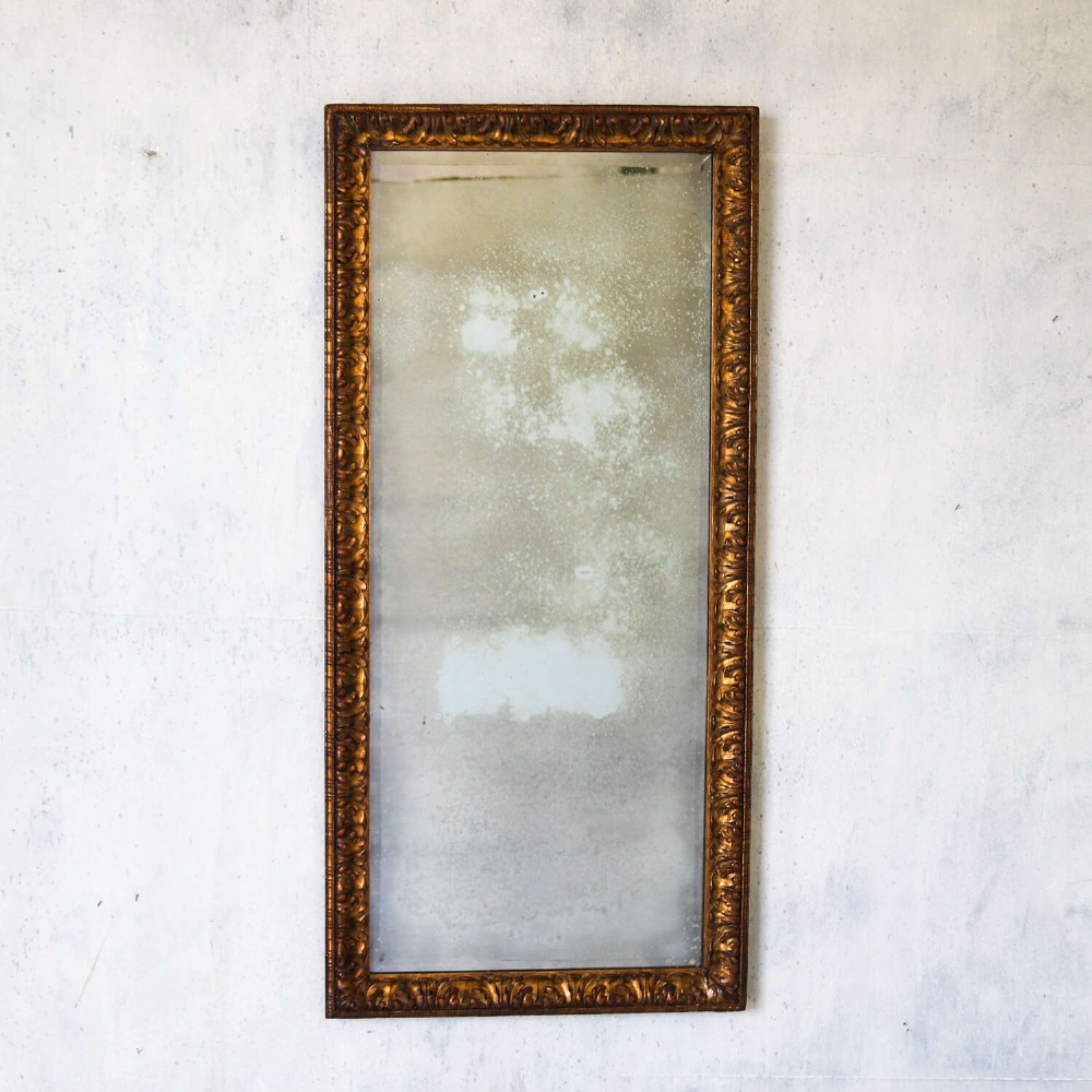 A tall rectangular nineteenth-century French mirror featuring a gilded wood frame with relief pattern molding and heavily foxed mirrored glass. View II