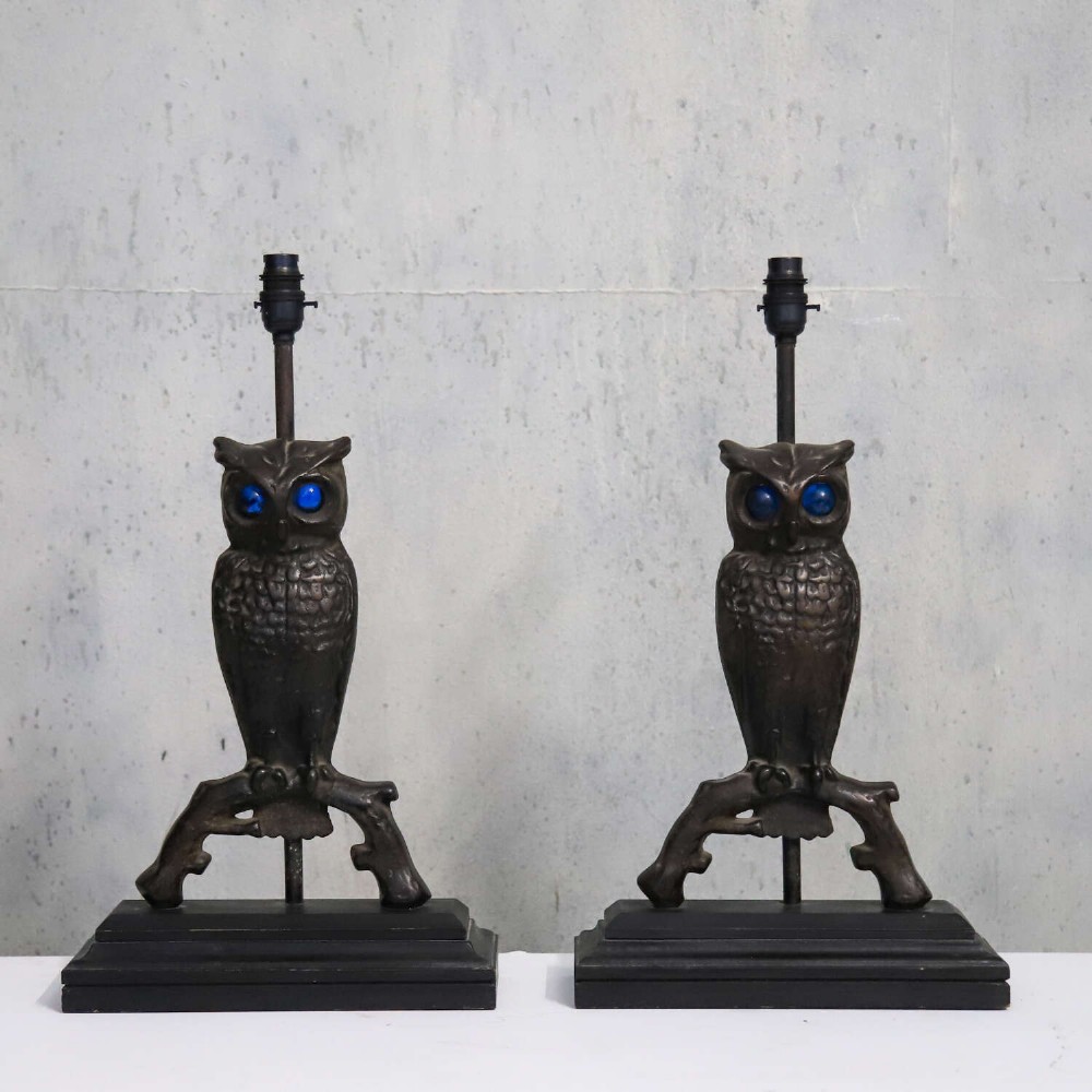 A pair of dark cast iron owl table lamps with bright blue glass eyes, perched on branch bases mounted on black plinths. View II