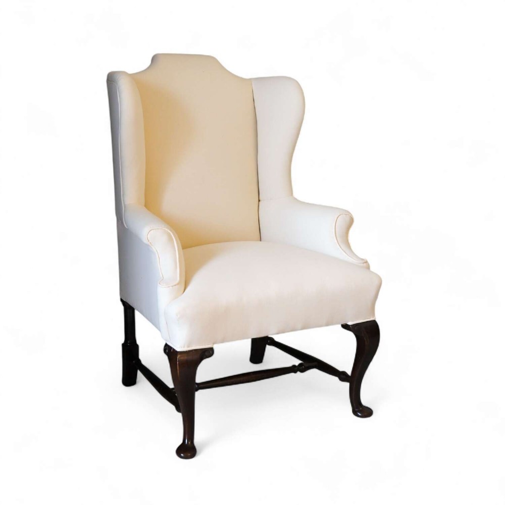 A 19th-century wingback armchair newly upholstered in plain cream calico fabric with dark carved timber cabriole front legs.