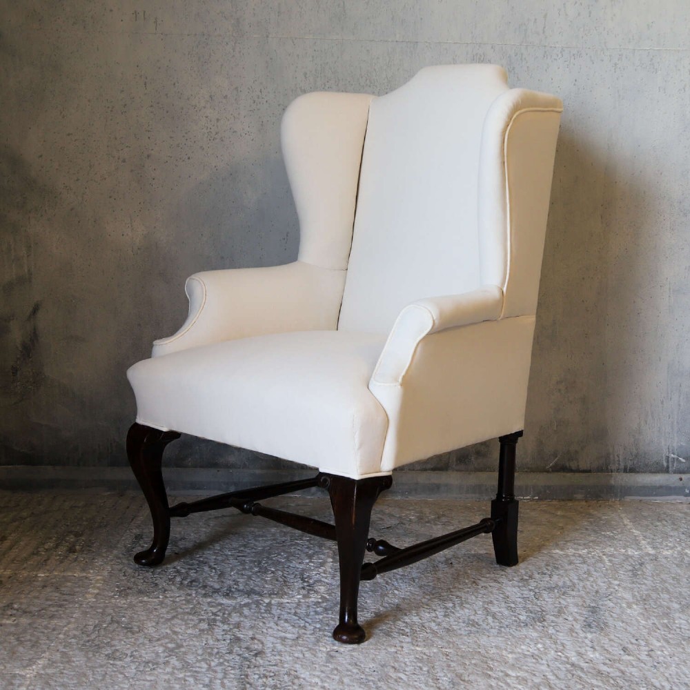 A 19th-century wingback armchair newly upholstered in plain cream calico fabric with dark carved timber cabriole front legs. View V