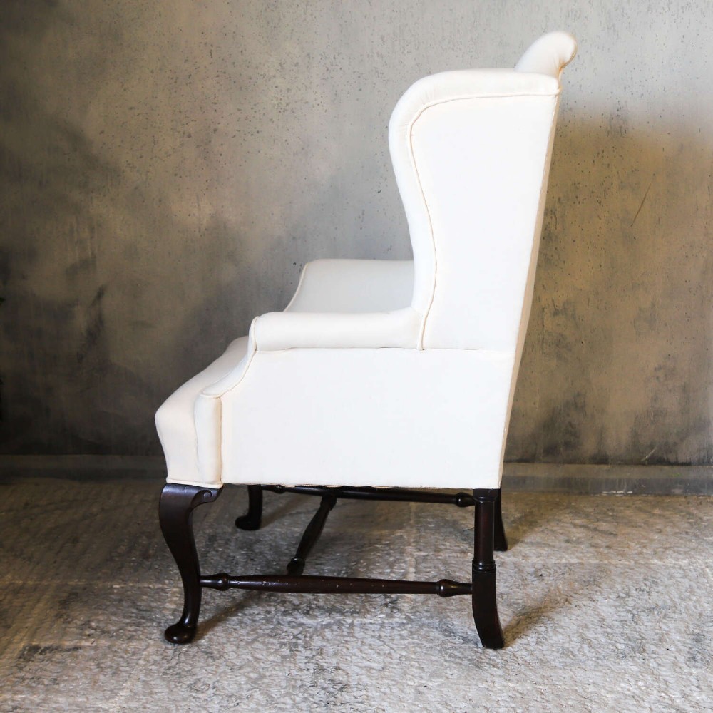 A 19th-century wingback armchair newly upholstered in plain cream calico fabric with dark carved timber cabriole front legs. View VI