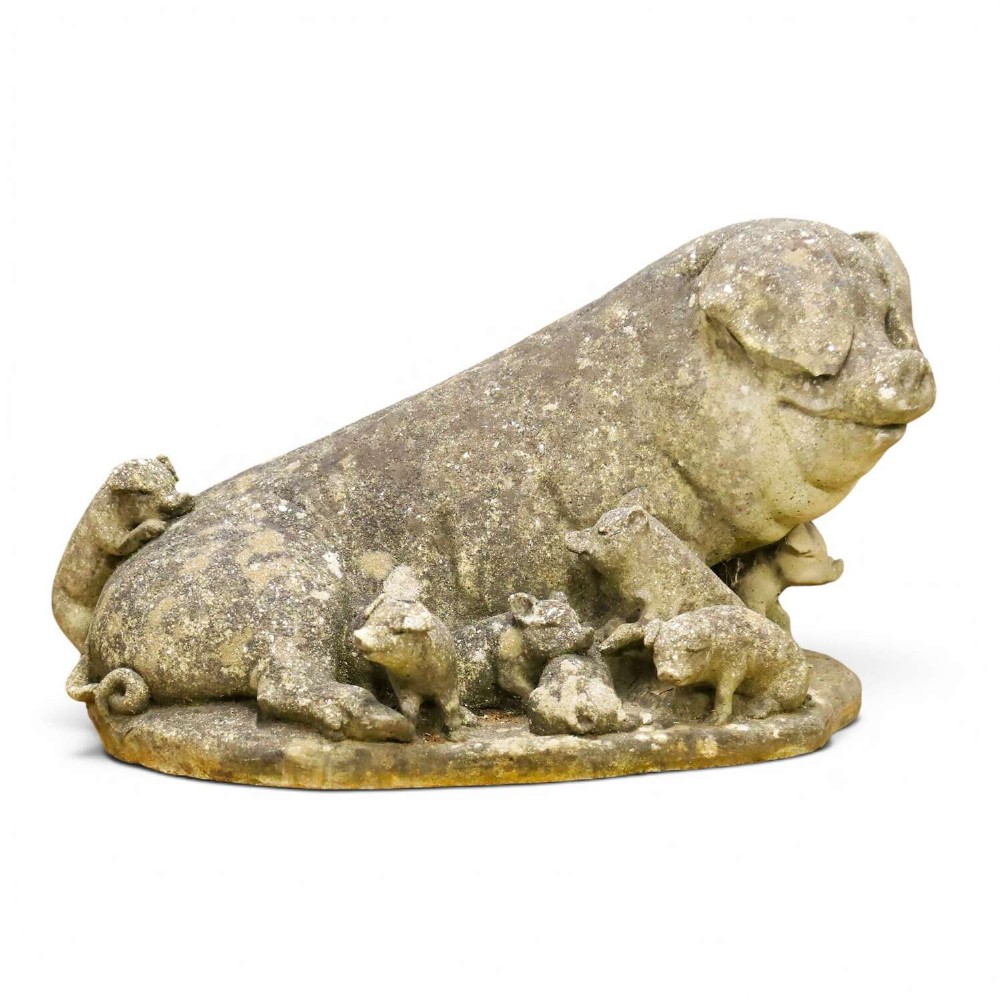 A weathered cast stone garden statue featuring a reclining sow flanked by seven small piglets on a moulded oval base.