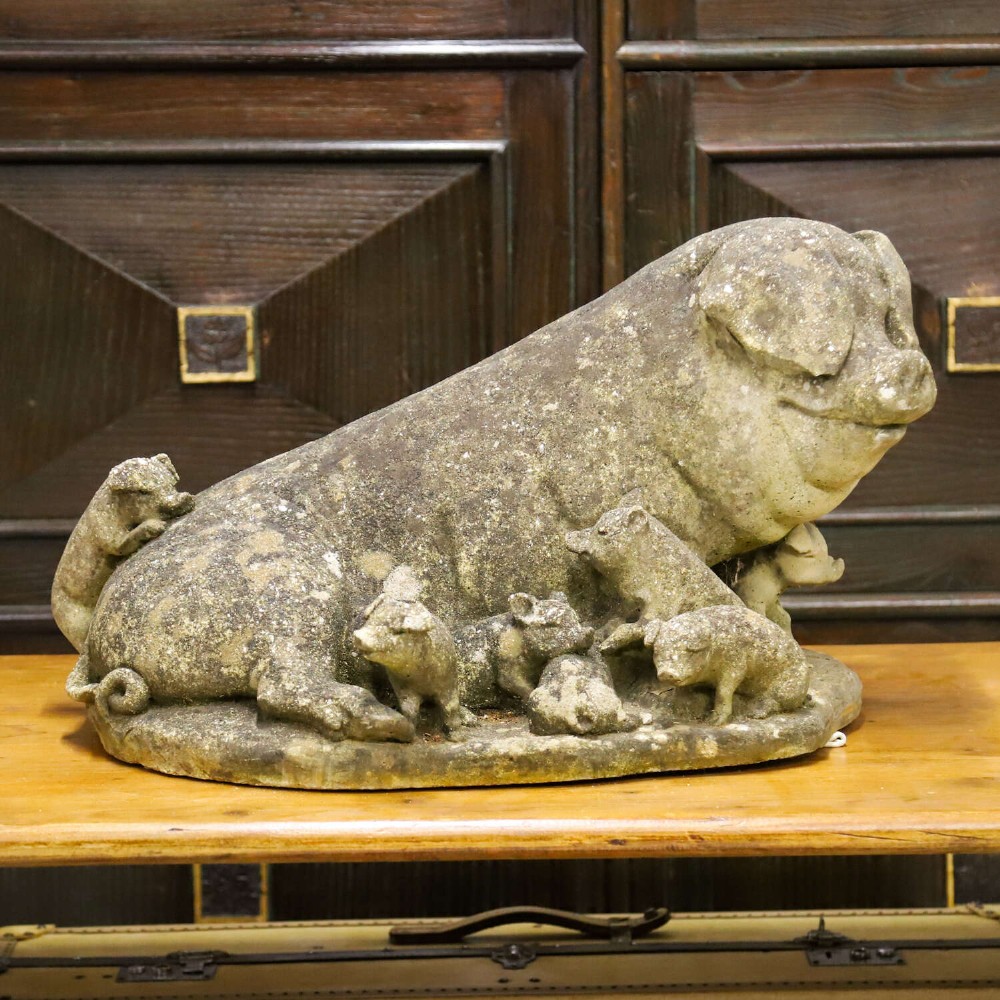 A weathered cast stone garden statue featuring a reclining sow flanked by seven small piglets on a moulded oval base. View II