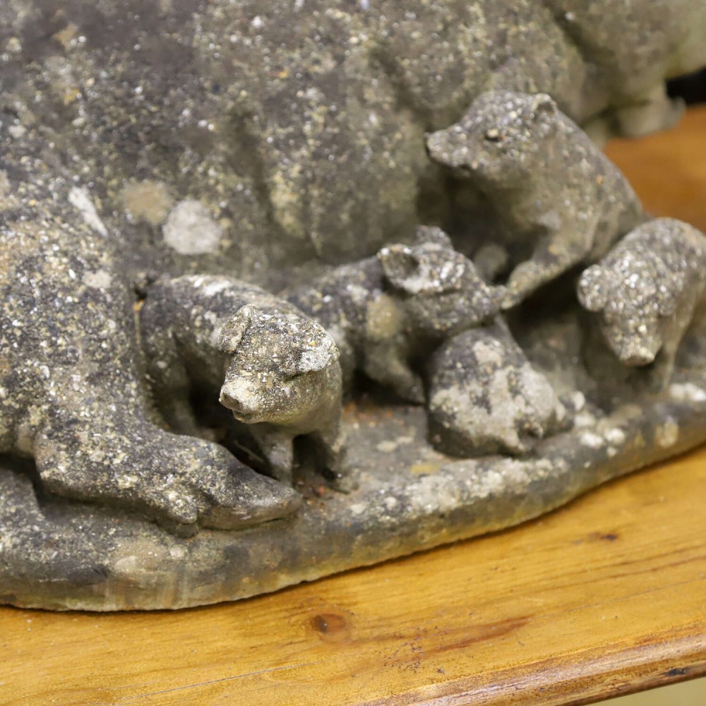 A weathered cast stone garden statue featuring a reclining sow flanked by seven small piglets on a moulded oval base. View IV