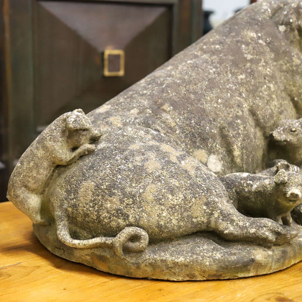 A weathered cast stone garden statue featuring a reclining sow flanked by seven small piglets on a moulded oval base. View V