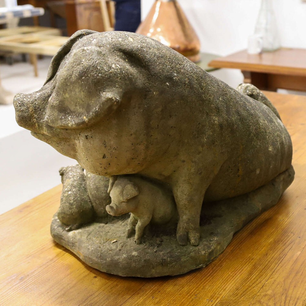 A weathered cast stone garden statue featuring a reclining sow flanked by seven small piglets on a moulded oval base. View VII