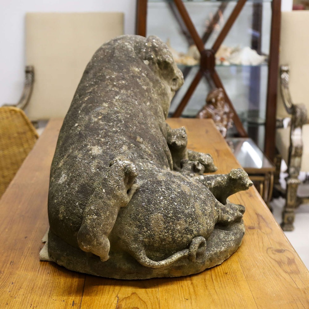 A weathered cast stone garden statue featuring a reclining sow flanked by seven small piglets on a moulded oval base. View VIII