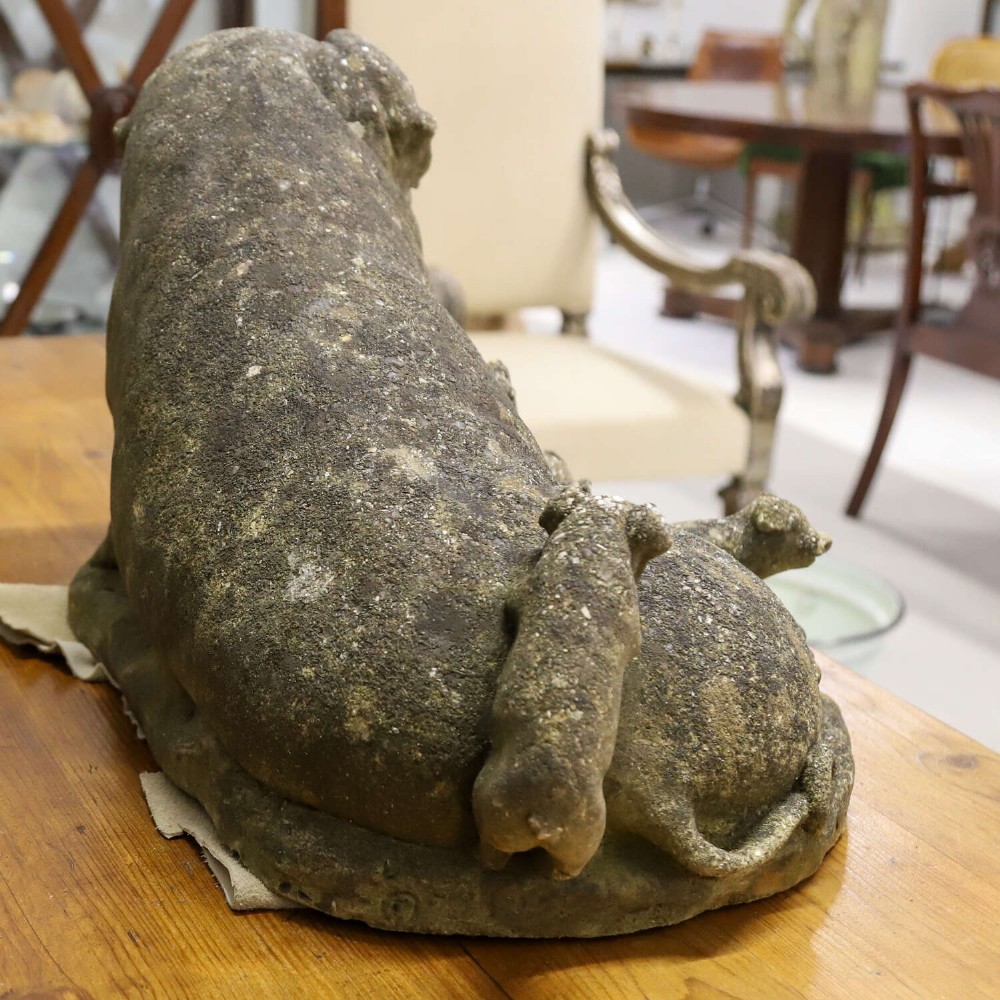 A weathered cast stone garden statue featuring a reclining sow flanked by seven small piglets on a moulded oval base. View IX