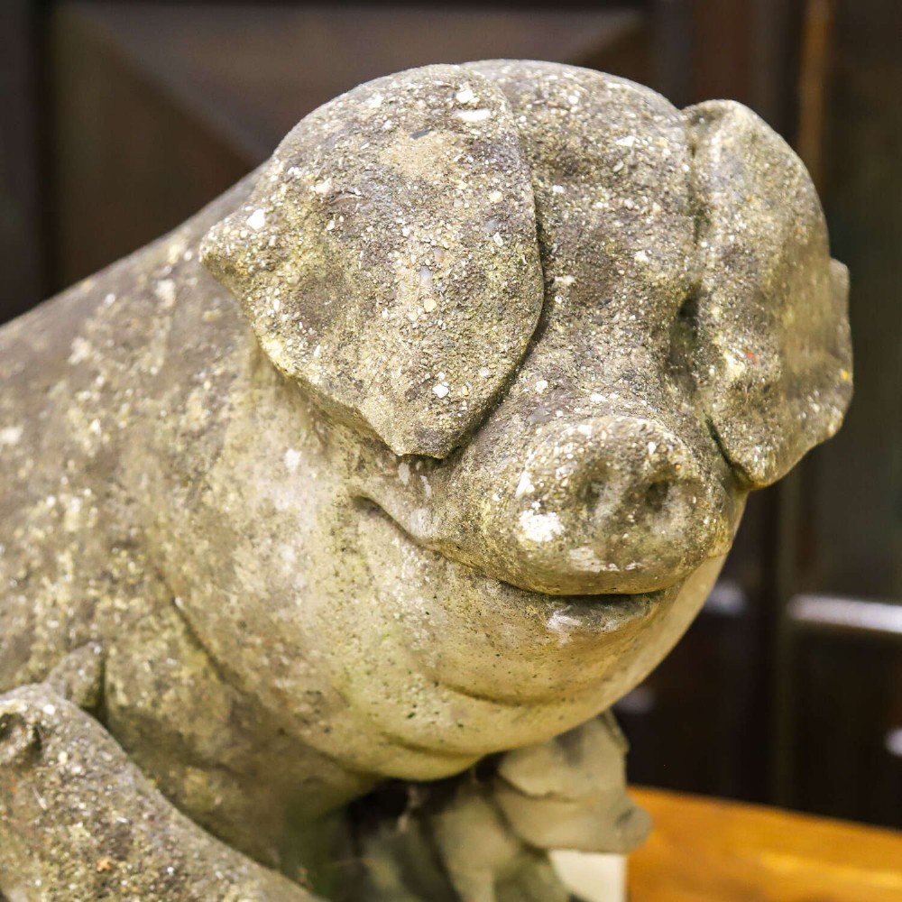 A weathered cast stone garden statue featuring a reclining sow flanked by seven small piglets on a moulded oval base. View X