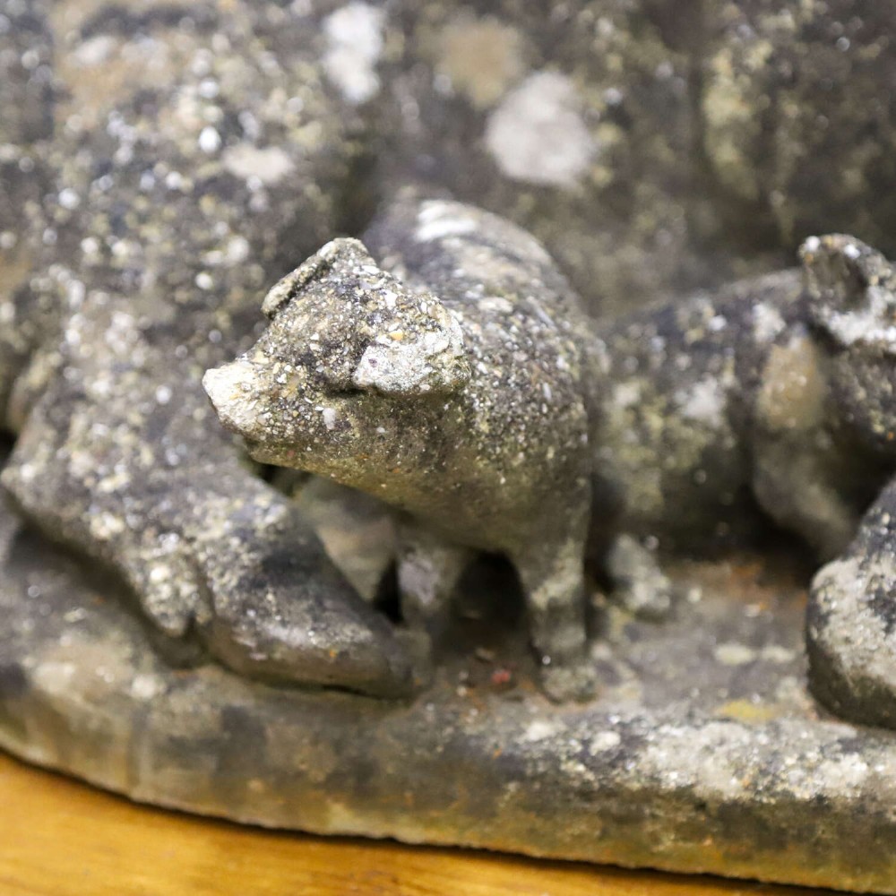 A weathered cast stone garden statue featuring a reclining sow flanked by seven small piglets on a moulded oval base. View XI