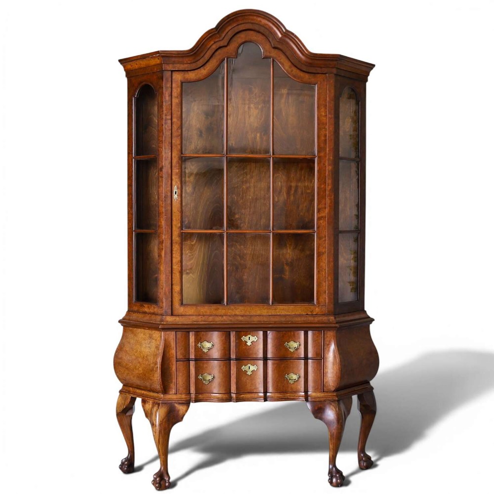 A Dutch walnut-veneered glazed cabinet featuring an arched top, glass paned upper doors, a shaped lower drawer section, and cabriole legs with claw and ball feet.