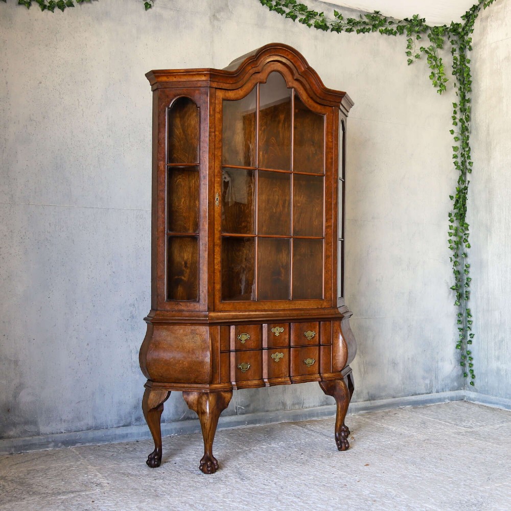 A Dutch walnut-veneered glazed cabinet featuring an arched top, glass paned upper doors, a shaped lower drawer section, and cabriole legs with claw and ball feet. View II