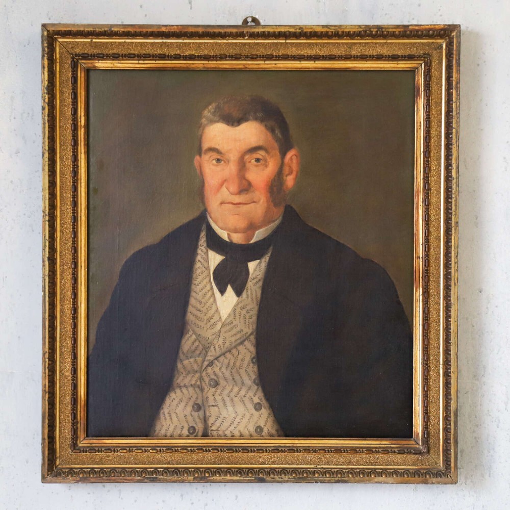 An antique oil painting depicting a male subject wearing a patterned waistcoat and black jacket, set in a gilded frame. View II