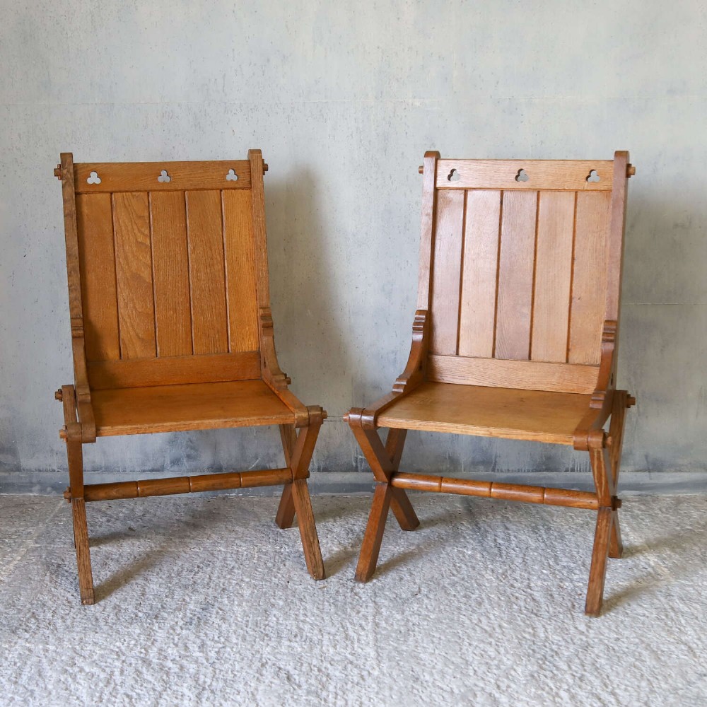A pair of warm brown oak Glastonbury chairs featuring panelled backs with trefoil cut-outs and exposed pegged X-frame legs. View II
