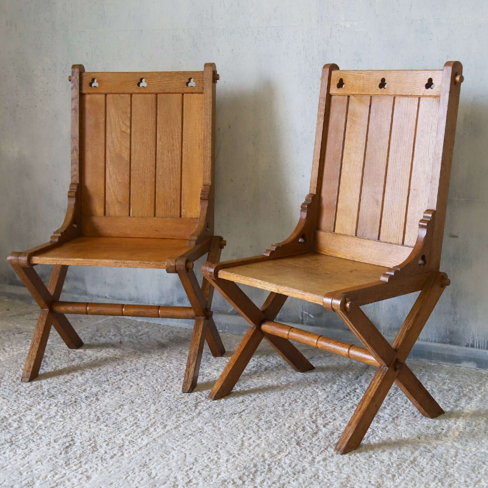 A pair of warm brown oak Glastonbury chairs featuring panelled backs with trefoil cut-outs and exposed pegged X-frame legs. View III