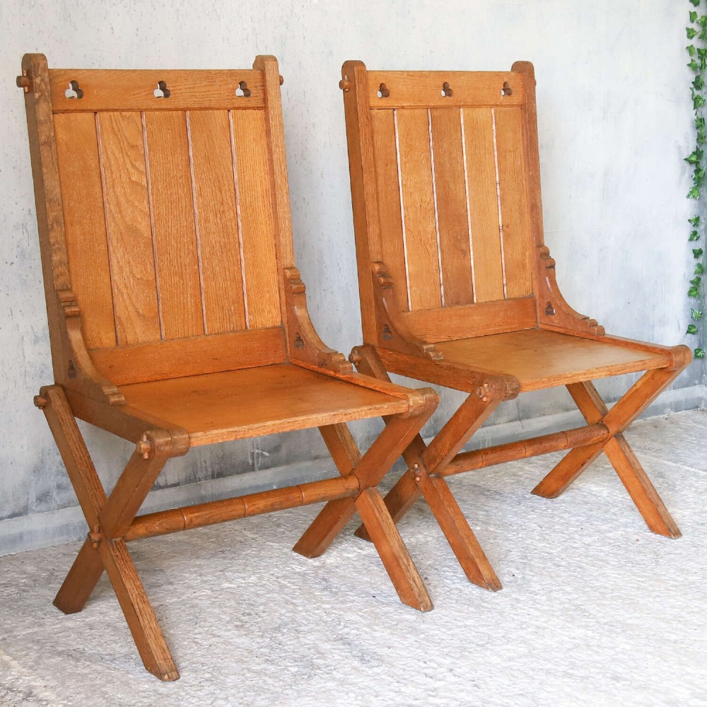 A pair of warm brown oak Glastonbury chairs featuring panelled backs with trefoil cut-outs and exposed pegged X-frame legs. View VI