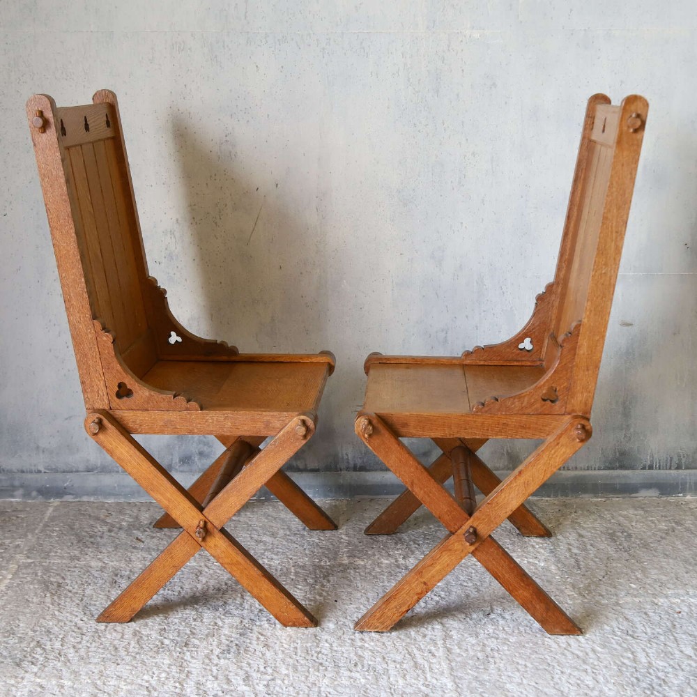 A pair of warm brown oak Glastonbury chairs featuring panelled backs with trefoil cut-outs and exposed pegged X-frame legs. View VIII